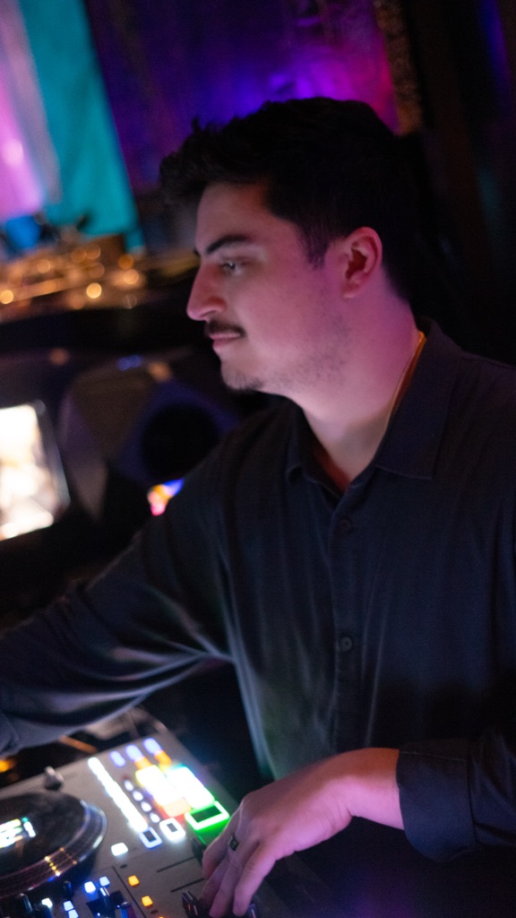 DJ OTEO profile at the deck, purple-amber club lighting, working at mixer