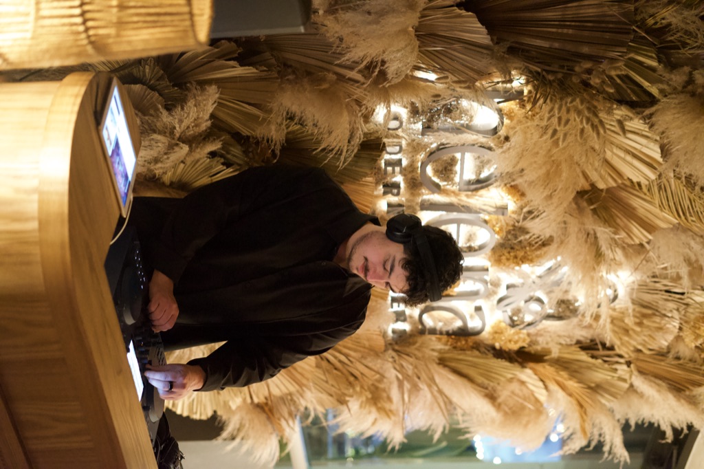 DJ OTEO at the deck, full Helena wordmark signage centered behind, working at the rotaries