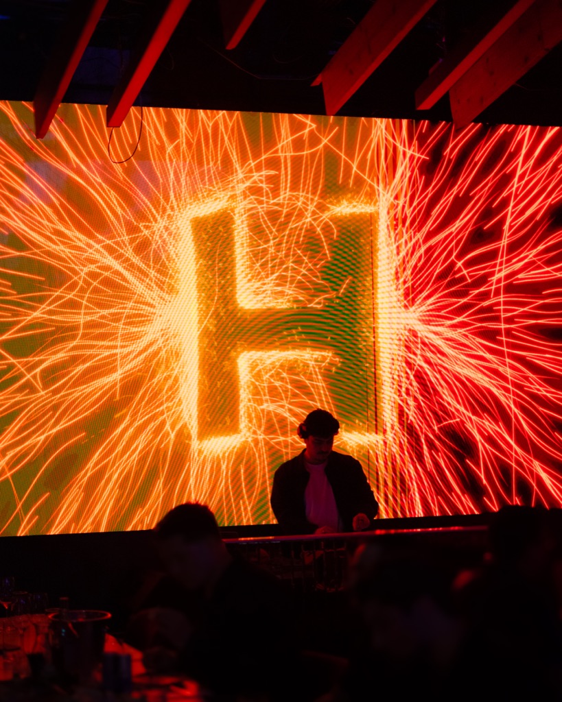 Massive fire-wirework H letterform projection behind DJ OTEO at the decks