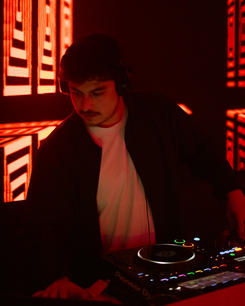 DJ OTEO close-up at Pioneer DJM mixer, red venue-light bath at The H
